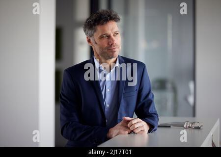 Besinnlicher Geschäftsmann, der im Büro am Schreibtisch steht Stockfoto