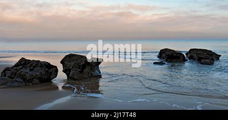 Farbfoto der Küstenfelsen am Strand einige geglättet und abgerundet durch die Passagen von Zeit und Flut mit Steinkobbeln und Kieselsteinen, die auf t liegen Stockfoto