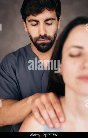 Physiotherapeutin mit geschlossenen Augen, die der Frau eine Massage auf der Schulter gibt Stockfoto