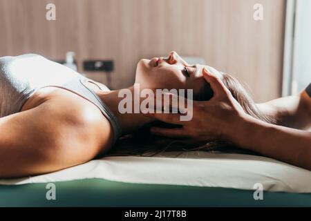 Frau mit geschlossenen Augen erhält Kopfmassage durch Physiotherapeutin in der medizinischen Klinik Stockfoto