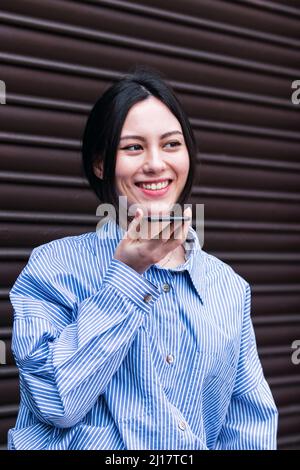 Lächelnde Frau, die über einen Lautsprecher vor dem Auslöser auf dem Smartphone spricht Stockfoto