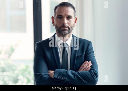 Porträt eines Geschäftsmannes, der mit gekreuzten Armen auf die Kamera schaut Stockfoto