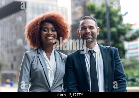 Porträt von zwei Geschäftskollegen, die nebeneinander stehen und die Kamera anlächeln Stockfoto