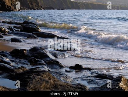Farbfoto der Küstenfelsen am Strand einige geglättet und abgerundet durch die Passagen von Zeit und Flut mit Steinkobbeln und Kieselsteinen, die auf t liegen Stockfoto