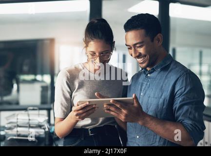 Es ist einfach, groß zu reden. Aufnahme von zwei jungen Mitarbeitern, die in einem modernen Büro ein digitales Tablet nutzen. Stockfoto