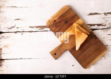 Blick von oben auf das frische Käsesandwich auf dem hölzernen Servierbrett über dem weißen Tisch Stockfoto