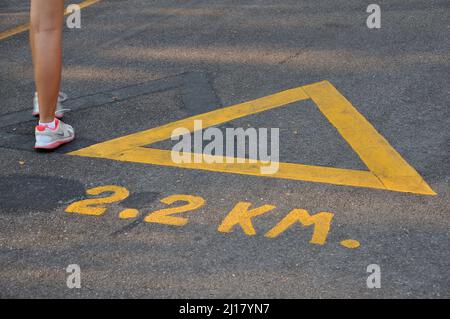 Joggingstrecke mit Meterzahl von 2,2 km, gelbes Farbsymbol, das die Distanz zum Joggen und Laufen aufzeigt, Joggingstrecke Asphalt Stockfoto