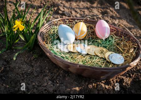 Verschiedene Krypto-Münzen liegen in einem osterkorb zusammen mit ostereiern nebeneinander Stockfoto