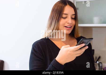 kaukasische junge Frau zu Hause, die im lauten Modus telefoniert, durch Chats in ihrem Haus, Lebensstil und Technologiekonzept kommuniziert. Stockfoto