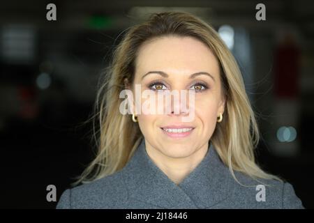 Attraktive blonde Frau mit einem reizenden, lebhaften Lächeln in einem frontalen Porträt mit Kopf und Schultern und Copyspace Stockfoto