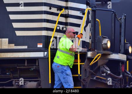 BENSENVILLE, Illinois, USA. Ein Arbeiter fährt auf den Stufen einer Lokomotive der Norfolk Southern Railway, die einen Güterzug der Canadian Pacific Railway führt. Stockfoto