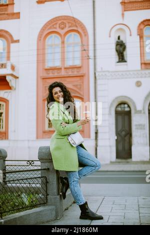 Hübsche junge Frau auf der Straße, die Kaffee zum Mitnehmen hält Stockfoto