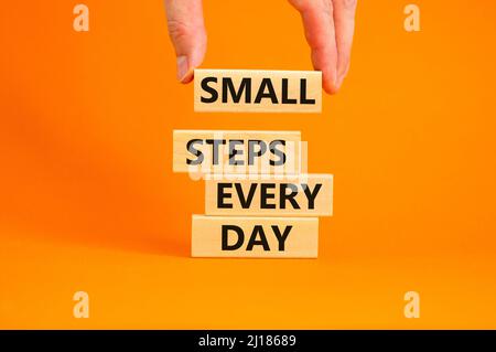 Symbol für kleine Schritte pro Tag. Konzept Worte kleine Schritte jeden Tag auf Holzblöcken. Geschäftsmann Hand. Schöne orange Tisch orange Hintergrund. Klein Stockfoto
