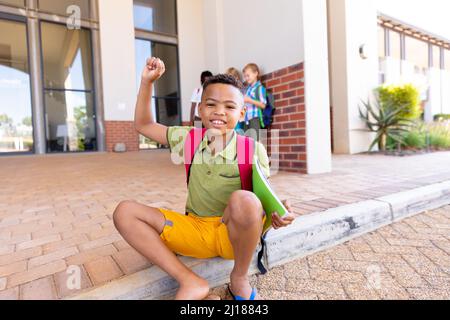 Porträt eines lächelnden biracial Grundschüler mit erhobener Hand sitzt auf dem Boden in der Schule Stockfoto