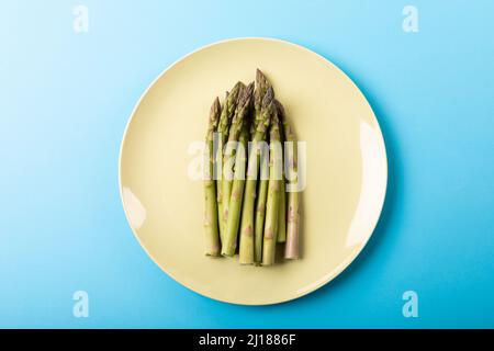 Direkt über Ansicht von frischem Spargel in weißem Teller auf blauem Hintergrund Stockfoto