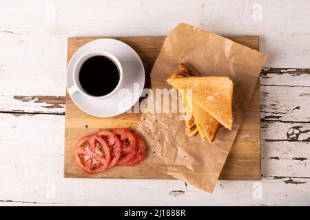 Blick von oben auf das Frischkäse-Sandwich mit Tomatenscheiben und schwarzem Kaffee auf dem Servierbrett Stockfoto