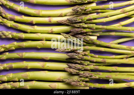 Vollbildaufnahme von rohem Gemüse mit grünem Spargel vor violettem Hintergrund. Unverfälscht, Lebensmittel, gesunde Ernährung und Bio-Konzept. Stockfoto