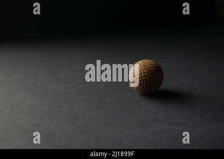 Alter Golfball auf der schwarzen Oberfläche mit schwarzem Hintergrund mit Licht und Schatten. Platz mit ausgewähltem Fokus kopieren. Stockfoto