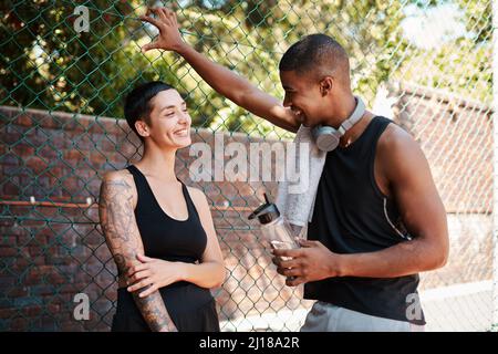 Ihre Chats sind immer fröhlich. Aufnahme zweier sportlicher junger Menschen, die sich im Freien gegen einen Zaun unterhalten. Stockfoto