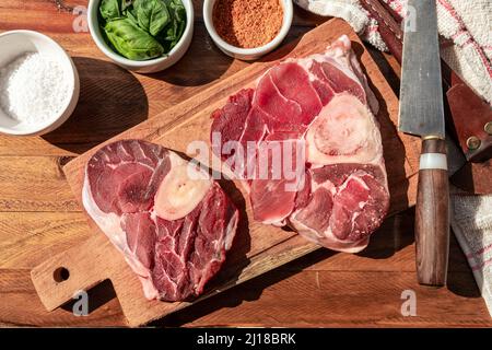 Zwei Steaks rohes Ossobuco-Rindfleisch auf einem Holzbrett mit Gewürzen zum Abschmecken der Fleischstücke. Tierisches Protein-Konzept, billige Fleischstücke. Aereal vie Stockfoto