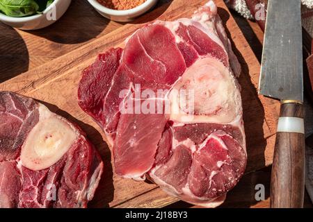 Ein frisches Ossobuco-Steak aus rohem Rindfleisch auf einem Brett mit Garnierungen auf einem Holztisch. Tierisches Protein-Konzept, italienische Lebensmittel. Aerealansicht Stockfoto