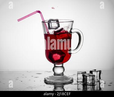 Kalter Tee, Cocktail, Fruchtgetränk in einer hohen Glasschale mit Trinkhalm auf einem Tisch mit Eisstücken auf einem weißen Hintergrund. Sommergetränke Stockfoto