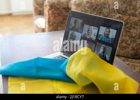 Flagge der Ukraine auf dem Hintergrund und breiten digitalen Bildschirm des Laptops mit Videokonferenz. Krieg mit Russland. Cyberangriff, Sanktionen, wirtschaftlicher Zusammenbruch Stockfoto