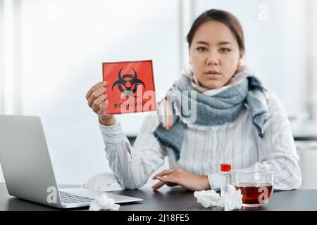 Wir alle sollten in dieser Krise sicherheitsbewusst sein. Aufnahme einer jungen Geschäftsfrau mit einem Biogefahrenschild an ihrem Schreibtisch in einem modernen Büro. Stockfoto