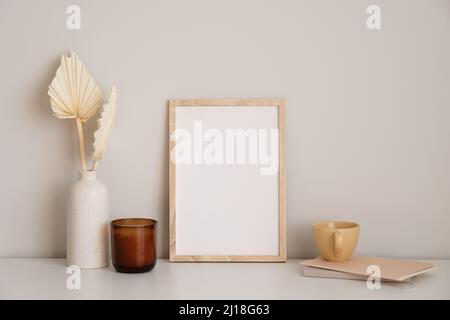 Schreibtisch im Wohnzimmer im nordischen Stil. Bilderrahmen-Mockup, Kerze, trockene Blumen in Vase, Tasse Tee, Papier Notizbuch auf weißem Tisch. Stockfoto