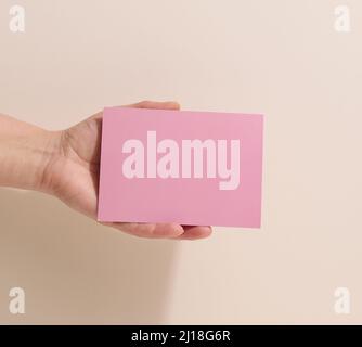 Weibliche Hand mit leerem rosa Papier auf beigem Hintergrund. Kopieren Bild oder Text einfügen, Nahaufnahme Stockfoto