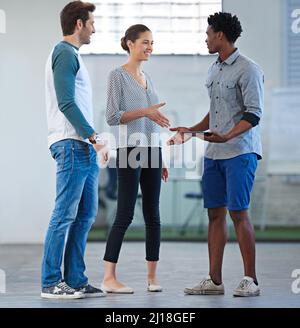 Unsere Teams sorgen dafür, dass es wirklich bleibt. Drei lässig gekleidete kreative Mitarbeiter treffen sich und begrüßen sich gegenseitig. Stockfoto