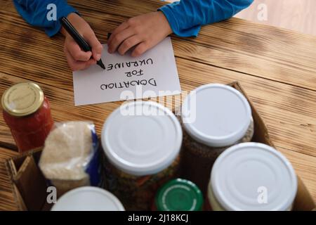 Eine Person, die eine Kiste mit Lebensmitteln vorbereitet, um dem Krieg in der Ukraine zu spenden. Stockfoto