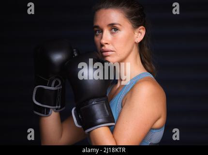 Unzerbrechlich und unbesiegt. Porträt einer jungen Frau mit Boxhandschuhen vor schwarzem Hintergrund. Stockfoto