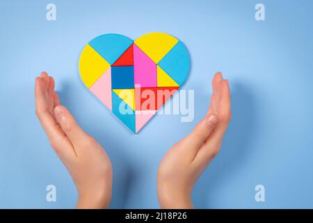 Kind Hände mit bunten Puzzle Herz auf hellblauem Hintergrund. Konzept des Welt-Autismus-Tages Stockfoto