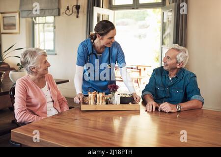 Das beste Frühstück gab es zusammen. Aufnahme einer jungen Krankenschwester, die während des Frühstücks in einem Pflegeheim ein Seniorenpaar aufgesucht hat. Stockfoto