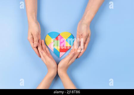 Konzept des Welt-Autismus-Tages. Erwachsene und Kinder Hände halten Puzzle Herz auf hellblauem Hintergrund. Draufsicht Stockfoto