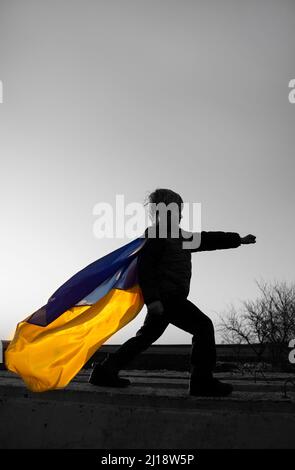 Schwarz-Weiß-Porträt des Jungen Superhelden mit einer winkenden ukrainischen Flagge in der Pose bereit für den Kampf, Hände in Fäusten. Farbakzent. Krieg stoppen. Bereit f Stockfoto