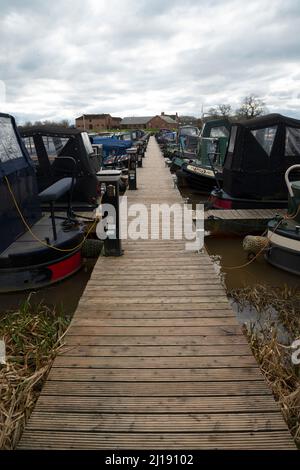 Ein Boardwalk-Steg an einem schmalen Yachthafen, mit Beleuchtung, elektrischem, Ankerplatz und Wasserstellen. Stockfoto