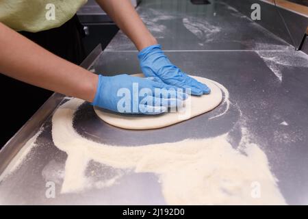 Teig mit männlichen Händen in blauen Gummihandschuhen auf Tischhintergrund machen. Der Pizzahersteller bereitet einen Pizzateig zu. Stockfoto