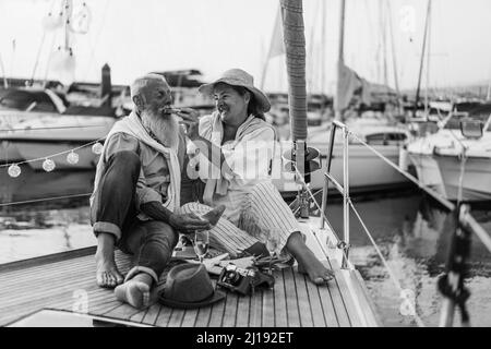 Ältere Paare haben Spaß beim Essen Früchte auf dem Segelboot - Fokus auf Frau Gesicht - Schwarz-Weiß-Ausgabe Stockfoto
