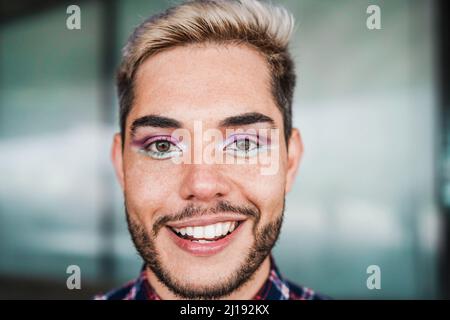 Junger Transgender-Mann mit Make-up lächelt vor der Kamera im Freien - Fokus auf Gesicht Stockfoto