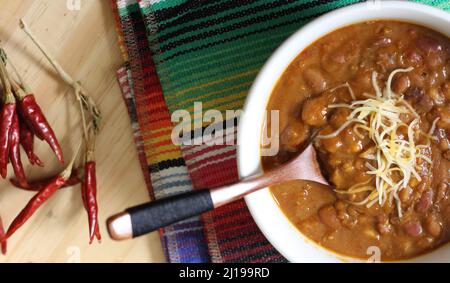 Schüssel Chili mit Pinto-Bohnen auf dem Tisch mit Paprika, Gewürzen und trockenen Bohnen im Hintergrund Stockfoto