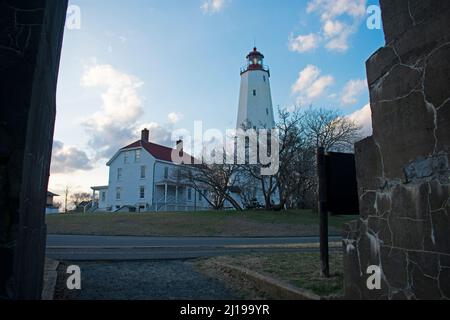 Leuchtturm in Sandy Hook, New Jersey, an einem teilweise sonnigen Tag im Spätwinter, von einer Öffnung in einer großen Steinmauer -63 aus gesehen Stockfoto