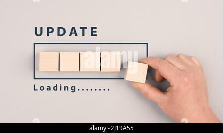 Die Wörter Update Loading stehen neben dem Fortschrittsbalken, Hand legt den letzten Würfel auf den Upload, grauer Hintergrund Stockfoto