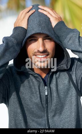 Hunk hält seinen Kopf warm. Porträt eines hübschen jungen Mannes, der einen Hoodie trägt und seinen Kopf hält. Stockfoto