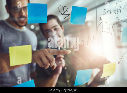 Sie sind voller großartiger Ideen. Eine kleine Aufnahme von zwei jungen Designern, die auf einer Glasplatine planen. Stockfoto