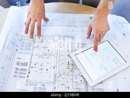 Gehen Sie durch das Design mit einem feinen Kamm. Aufnahme einer Architektenhand, die Baupläne untersucht und ein digitales Tablet verwendet. Stockfoto