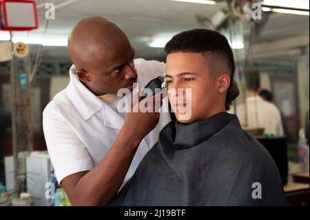 Ein Barbier trimmt die Haare eines jungen Mannes in einem Friseursalon in Havanna, Kuba. Stockfoto