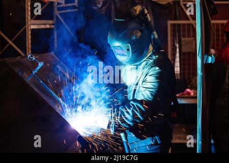 Fabrikarbeiter in Schutzmaske Schweißen Eisenteile. Stockfoto