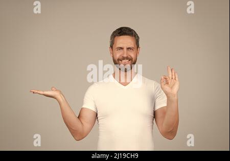 Glücklich Kerl zeigen offene Hand machen OK Ring Geste grauen Hintergrund kopieren Raum, Präsentation Produkt Stockfoto